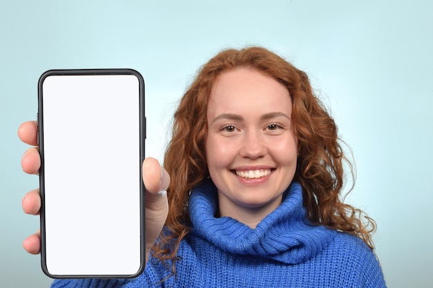 Linda mujer pelirroja mostrando smartphone con pantalla blanca en blanco