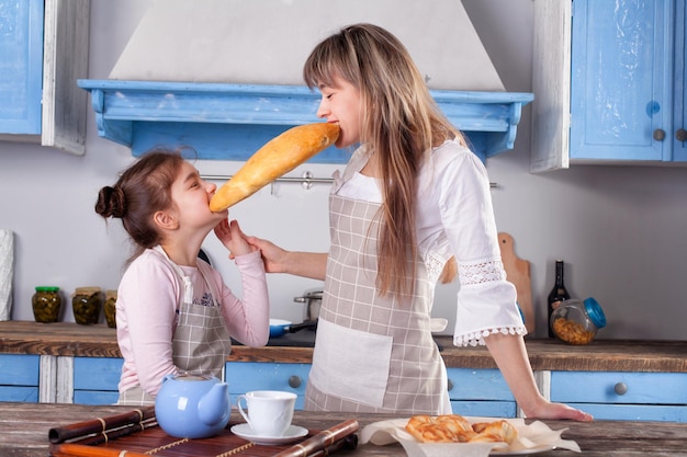 Linda mujer y pequeña adorable hija de pie en la mesa en la cocina cocinan juntos preparar