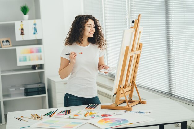 La linda mujer con un pincel pintando un cuadro en el caballete