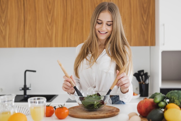 Una linda mujer rubia está preparando una ensalada en la cocina.