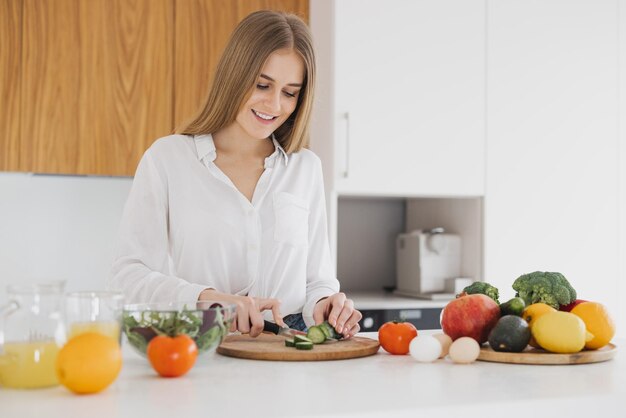 Una linda mujer rubia está preparando una ensalada en la cocina.