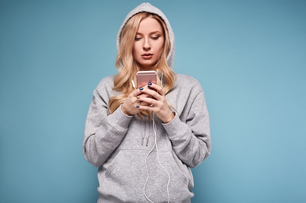 Linda mujer rubia positiva con capucha escuchando música