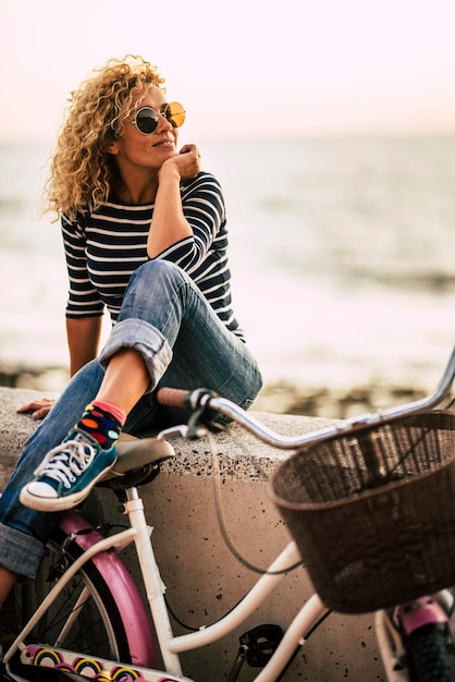 Linda mujer sentada al aire libre con una bicicleta relajada actividad de ocio con playa en el fondo Una mujer estilo de vida ciclista saludable Medio ambiente de transporte y sostenibilidad Felicidad libertad