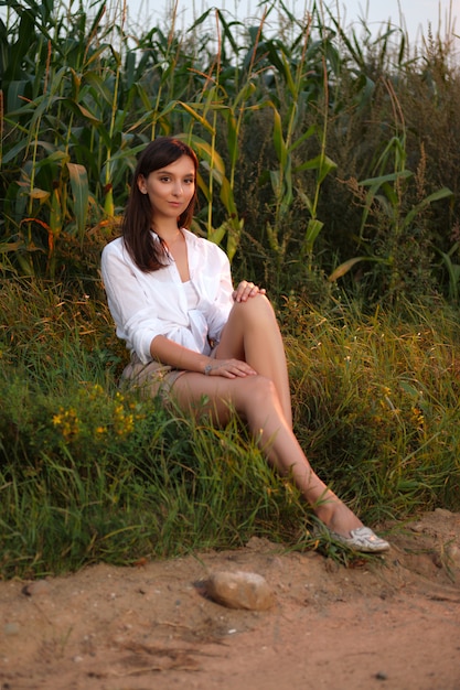 Linda mujer sentada al borde del camino rural en puesta de sol