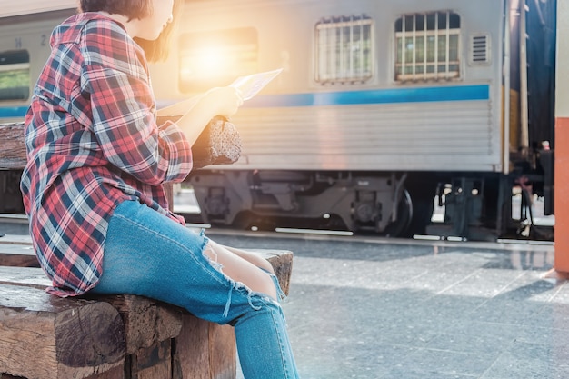 Linda mujer sentada con mapa. bolsa de viaje en la estación de tren