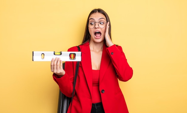 Linda mujer sintiéndose feliz, emocionada y sorprendida. arquitecto con un nivel