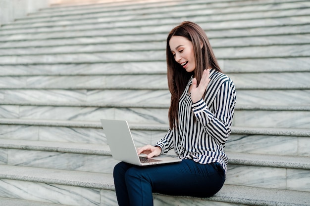 Linda mujer sonriendo y agitando su mano a la computadora portátil