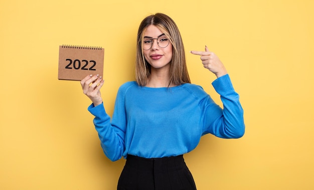 Linda mujer sonriendo con confianza apuntando a su propia amplia sonrisa. concepto de calendario 2022