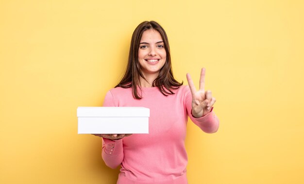 Linda mujer sonriendo y luciendo amigable, mostrando el número dos. concepto de embalaje de caja blanca