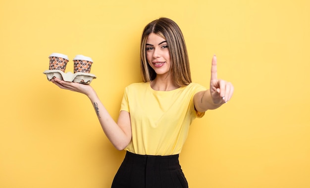 Linda mujer sonriendo con orgullo y confianza haciendo el número uno. concepto de cafés para llevar