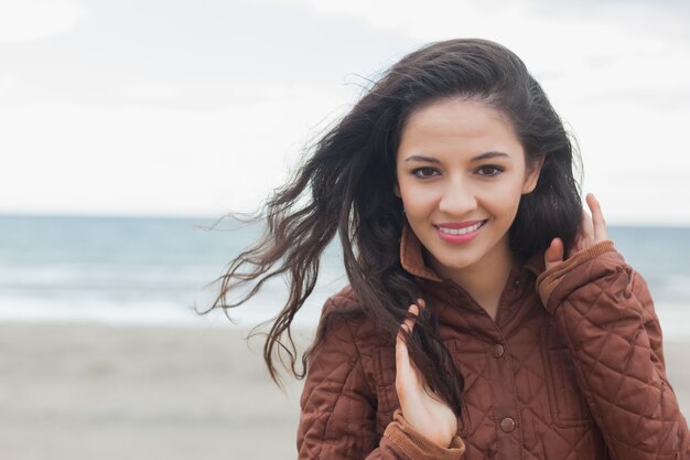 Linda mujer sonriente en elegante chaqueta marrón en la playa