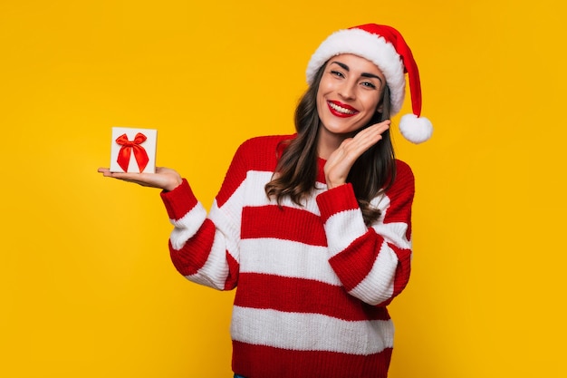 Linda mujer sonriente emocionada con caja de regalo de Navidad en las manos se divierte mientras posa sobre fondo amarillo