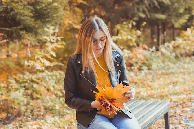 Linda mujer sonriente sosteniendo hojas de otoño en el concepto de ocio y estilo de vida estacional del parque de otoño