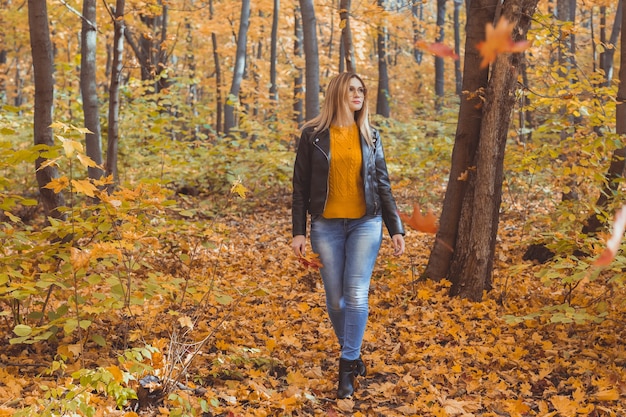 Linda mujer sonriente sosteniendo hojas de otoño y paseos en el ocio y el estilo de vida estacional del parque de otoño