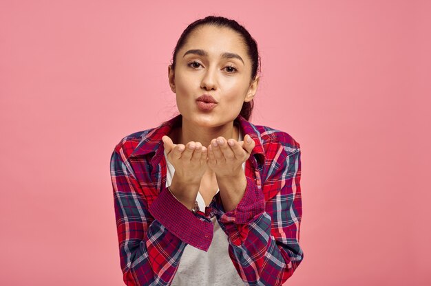 Linda mujer sopla un beso, pared rosa, emoción. Expresión facial, persona femenina mirando a cámara en estudio, concepto emocional, sentimientos