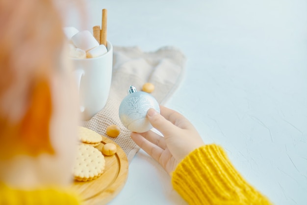 Linda mujer sosteniendo una bola de Navidad para decoración y chocolate caliente malvavisco canela