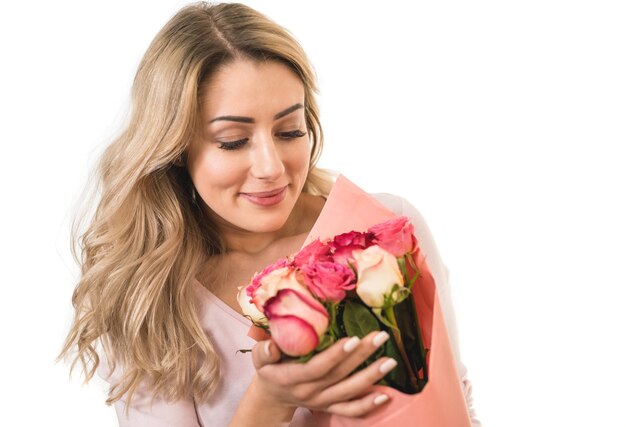 La linda mujer sostiene un ramo de flores sobre el fondo blanco.