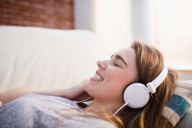 Linda mujer tendida en el sofá escuchando música en la sala de estar