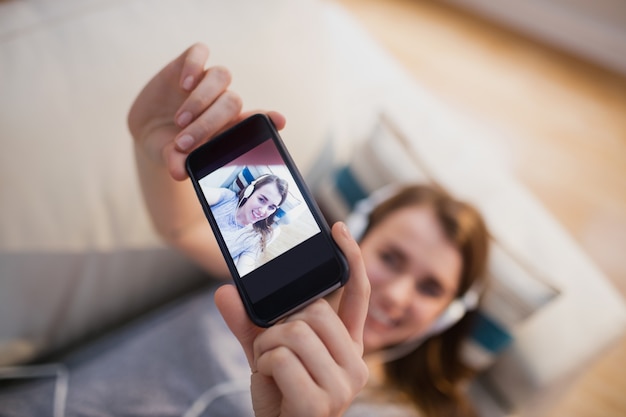 Linda mujer tendida en el sofá tomando selfie mientras escucha música en la sala de estar