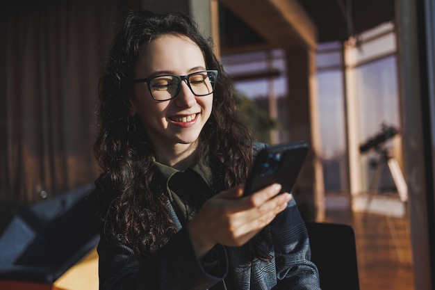 Una linda mujer trabaja en una computadora portátil en un café Joven mujer morena concentrada con gafas sentada en la mesa cerca de la ventana tomando café Trabajo independiente y remoto Estilo de vida moderno de la mujer