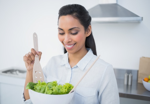 Linda mujer tranquila preparando ensalada de pie en la cocina