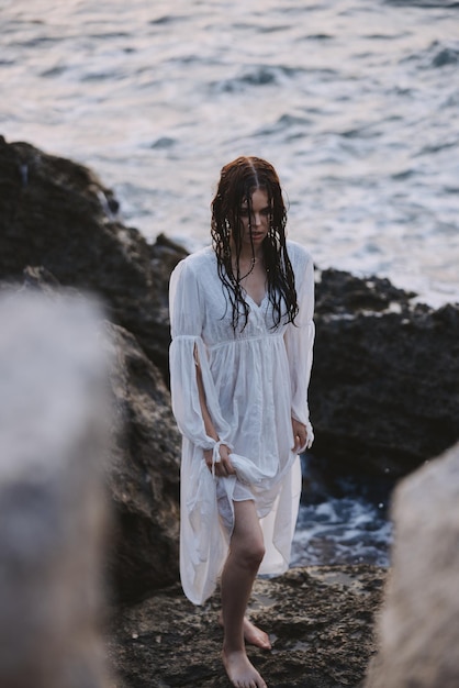 Linda mujer en vestido blanco se encuentra en las rocas océano naturaleza libertad