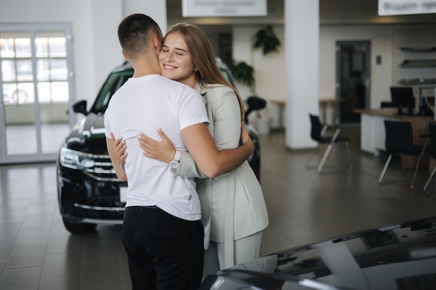 Linda mulher abraça seu marido depois de comprar carro no showroom de carros homem e mulher compram carro novo feliz