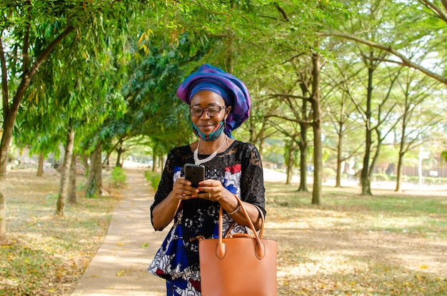 Linda mulher africana ao ar livre usando máscara facial se sentindo animada com o que viu em seu telefone