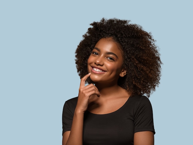 Foto linda mulher africana camiseta preta retrato corte de cabelo afro tocando seu rosto cor de fundo azul