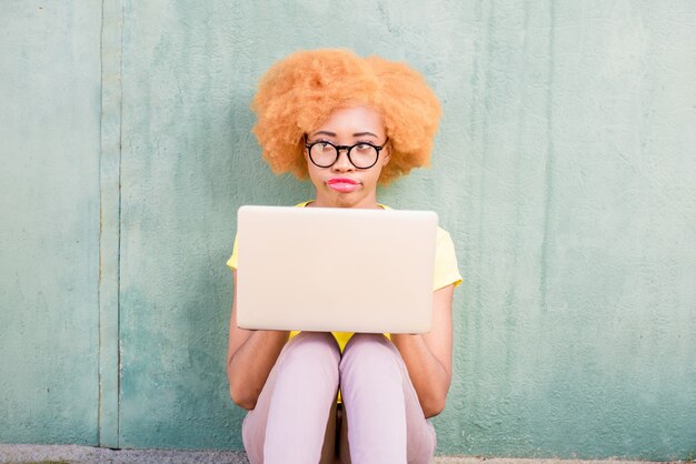 Linda mulher africana com cabelo encaracolado trabalhando com laptop sentado no fundo da parede verde