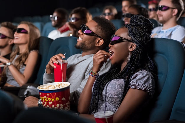 Foto linda mulher africana em óculos 3d, comendo pipoca enquanto estava em um encontro com o namorado no cinema