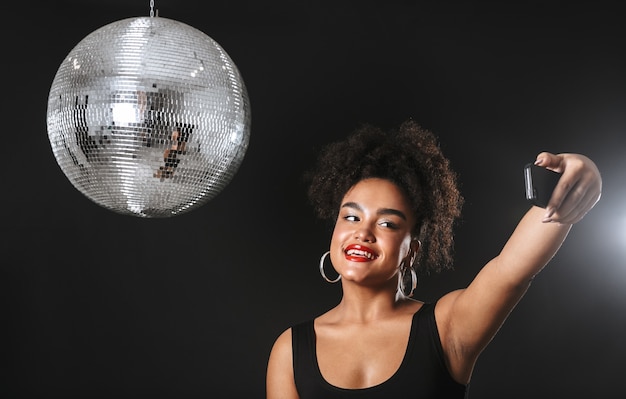 Linda mulher africana em pé com uma bola de discoteca prateada isolada no espaço negro