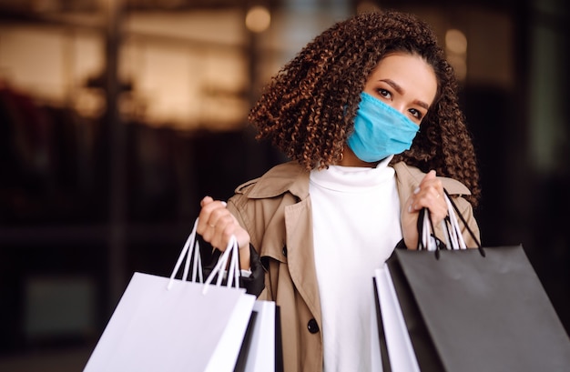 Linda mulher afro-americana com máscara protetora depois de fazer compras perto da loja