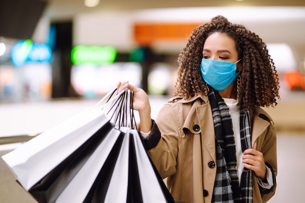 Foto linda mulher afro-americana com máscara protetora depois de fazer compras perto da loja