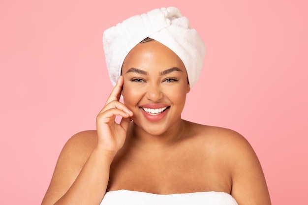 Linda mulher afro-americana de tamanho grande com toalha branca na cabeça, curtindo sua beleza jovem e sorrindo para a câmera