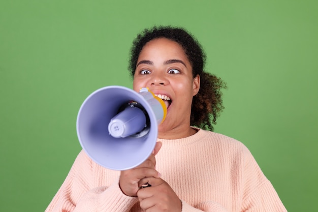 Linda mulher afro-americana na parede verde gritando e gritando no megafone, pedindo atenção