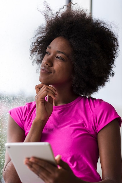 linda mulher afro-americana usando computador tablet em casa enquanto a chuva e o mau tempo estão ao ar livre