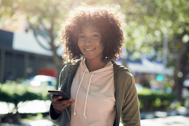 Linda mulher afro-americana usando smartphone sorrindo parecendo confiante na rua da cidade em dia ensolarado