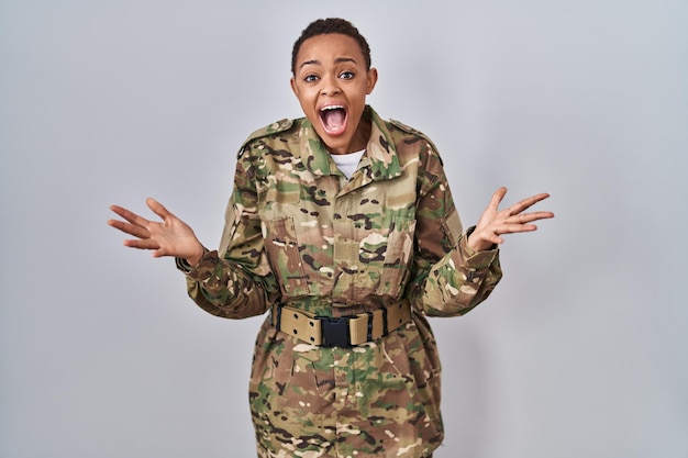 Linda mulher afro-americana vestindo uniforme do exército de camuflagem comemorando louco e espantado pelo sucesso com os braços levantados e olhos abertos gritando animado. conceito de vencedor