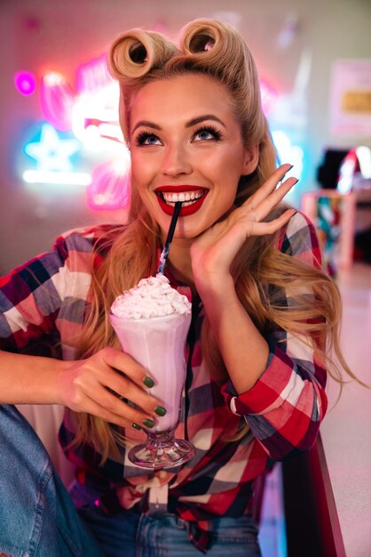 linda mulher alegre com um lindo penteado bebendo milkshake e sorrindo no café americano retrô