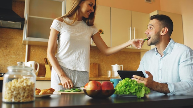 Linda mulher alimenta o marido enquanto cozinha o café da manhã