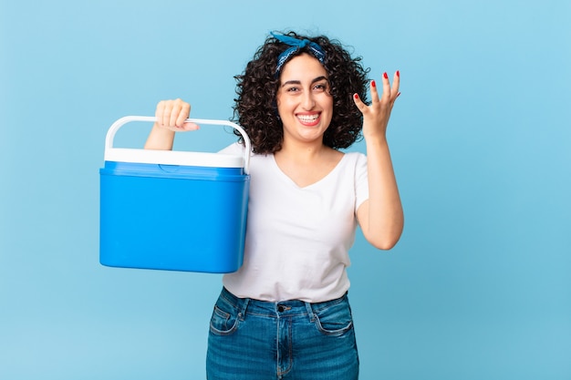 Linda mulher árabe se sentindo feliz e surpresa ao perceber uma solução ou ideia e segurando uma geladeira portátil