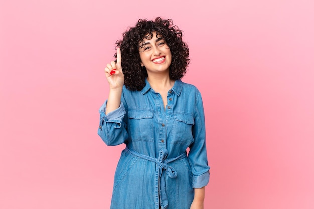 Linda mulher árabe sorrindo e parecendo amigável, mostrando o número um