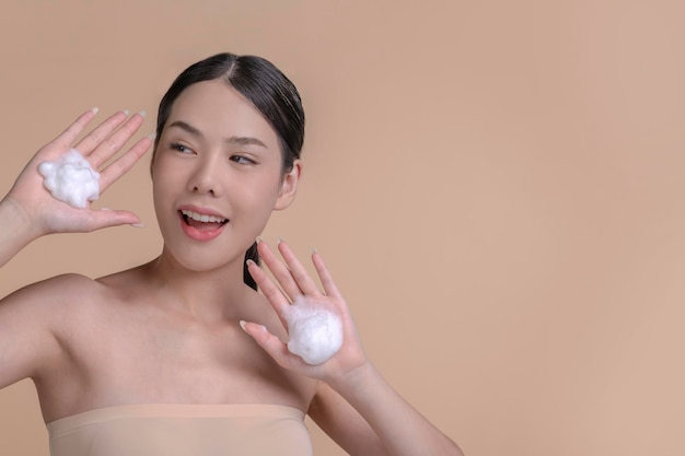 Linda mulher asiática aplicando creme hidratante Foto de mulher sorridente com maquiagem perfeita em fundo bege Conceito de beleza