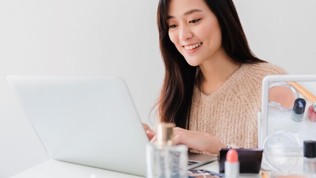 Linda mulher asiática blogger está conversando como fazer e usar cosméticos.