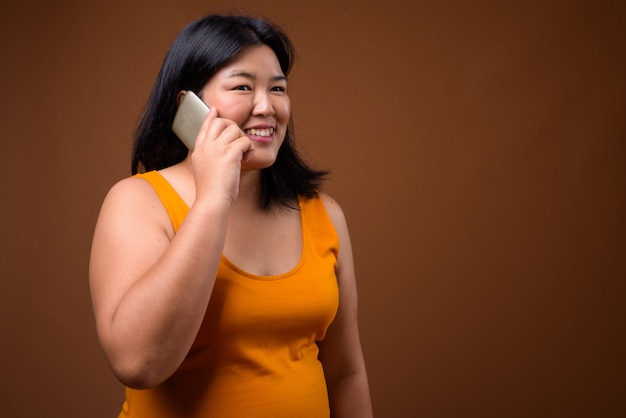 linda mulher asiática com excesso de peso usando vestido laranja sem mangas em marrom