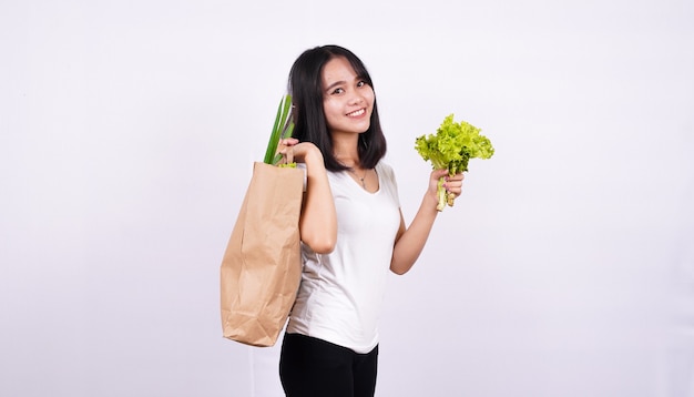 Linda mulher asiática com um saco de papel de vegetais frescos e segurando uma alface fresca com uma superfície branca isolada