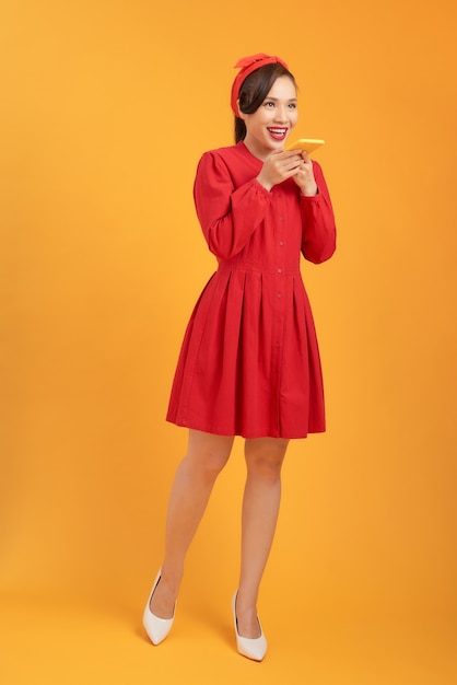 Linda mulher asiática com um vestido vermelho de pé sobre um fundo laranja