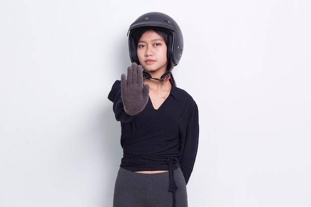 linda mulher asiática com uma mão aberta de capacete de motocicleta fazendo o sinal de stop com expressão séria