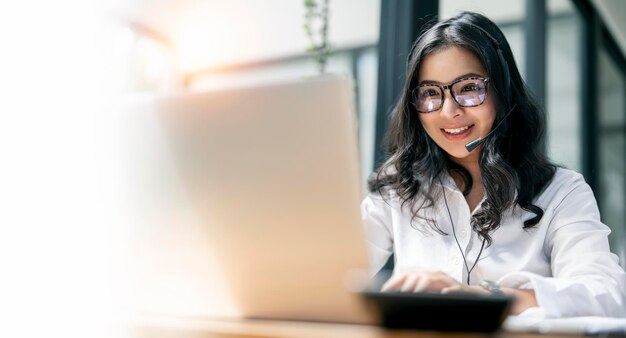 Linda mulher asiática com videochamada de fone de ouvido via laptop no escritório doméstico